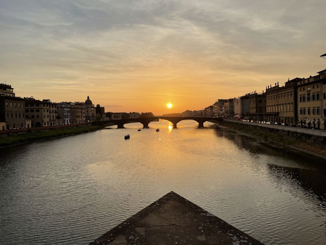 Sunset over the Arno river in Florence, bridges silhouetted against a gold sky.