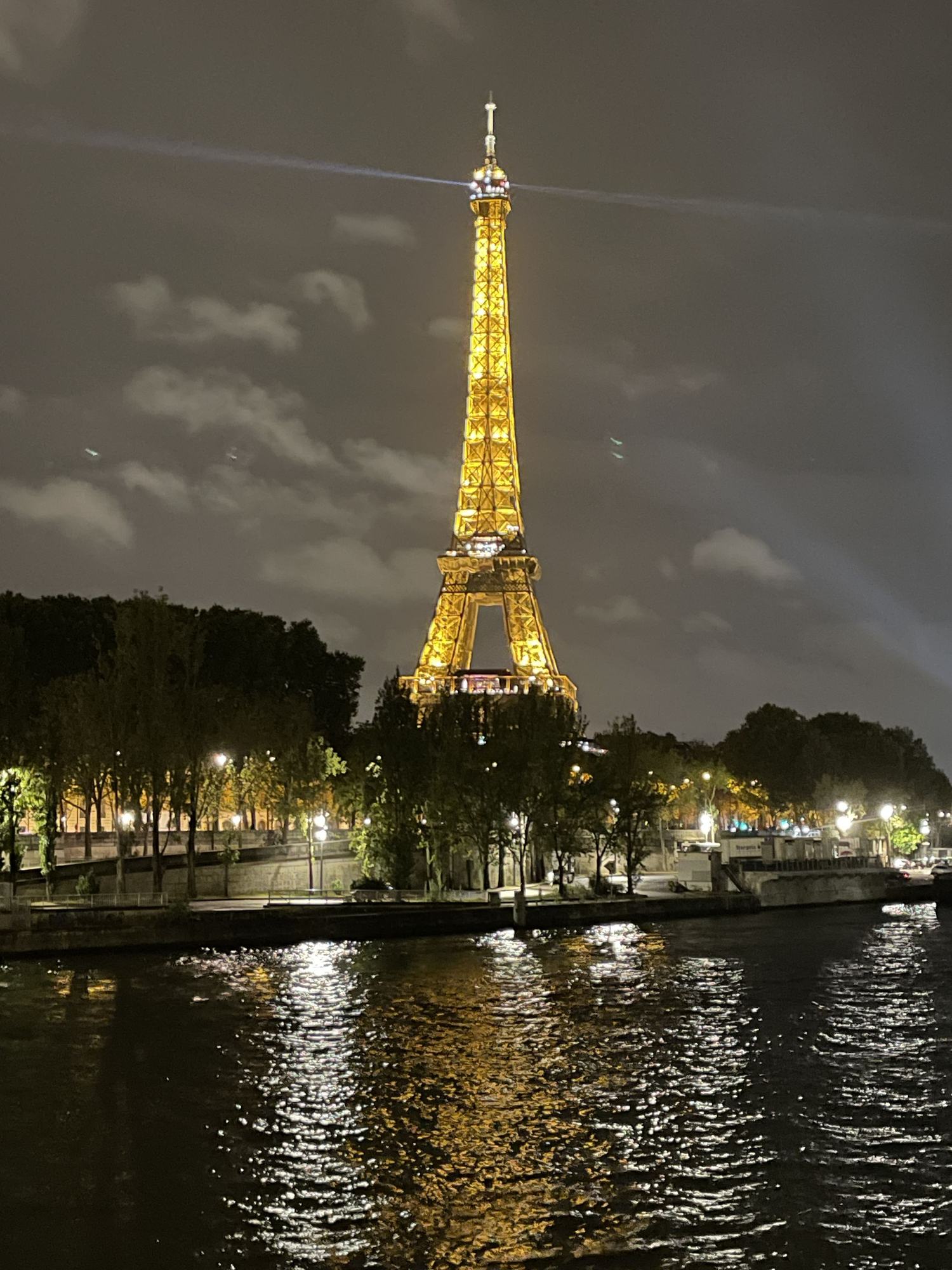 The Eiffel Tower lit gold at night, reflected in the Seine.